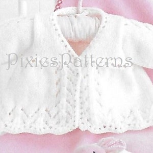 Op de afbeelding: Een wit gebreid babyvest met een delicaat kantpatroon en een knoopsluiting aan de voorkant. Het vest is afgebeeld op een roze achtergrond.