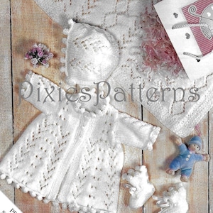 May include: White crocheted baby outfit with a lacy pattern. The outfit includes a bonnet, a dress, and booties. The outfit is laid out on a wooden surface.  The text "PREMATURE SIZE INCLUDED" is visible in the image.