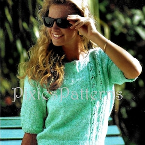 May include: A teal blue knitted sweater with a cable knit design and short sleeves. The sweater has a button closure at the neckline. The model is wearing the sweater with a white skirt.