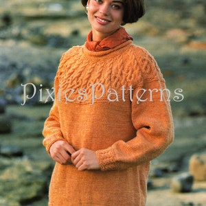May include: A close-up of a knitted orange sweater with a cable knit pattern. The sweater has a round neckline and long sleeves. The sweater is being worn by a person with short brown hair. The text "Pixies Patterns" is visible on the sweater.