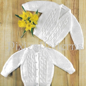 以下が含まれることがあります： ケーブル編みのディテールとボタン留めが施された、2つの白いニットベビーカーディガン。木製の表面に、黄色の水仙のブーケと一緒に展示されています。「PixiesPatterns」の文字が見えます。