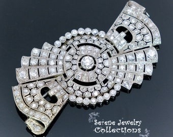 May include: A large, intricate diamond brooch with a geometric design. The brooch is made of platinum and features a central round diamond surrounded by smaller diamonds. The brooch is set in a geometric pattern of diamonds.