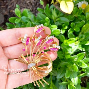 May include: A gold brooch with a bow design and pink and white stones. The brooch is set against a green background.
