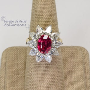 Può includere: Un anello con rubino rosso e una montatura a forma di fiore di diamanti più piccoli. L'anello è in oro giallo.
