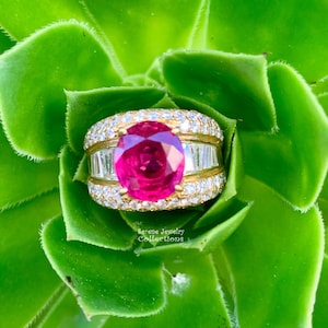 Può includere: Un anello d'oro con un grande rubino rosa vibrante circondato da un'aureola di diamanti più piccoli. L'anello è incastonato con diamanti baguette sulla fascia.