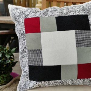 Könnte beinhalten: Ein weißes Kissen mit einem schwarz-weißen Muster an der Kante. Die Vorderseite des Kissens ist aus Patchwork-Stoff in den Farben Rot, Schwarz, Weiß und Grau.