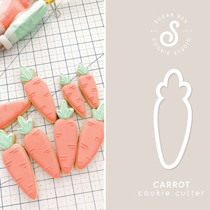May include: A set of ten orange carrot-shaped sugar cookies decorated with green leaves and white lines. The cookies are arranged on a white gridded surface. A cookie cutter in the shape of a carrot is shown on the right side of the image. The text "CARROT cookie cutter" is below the cookie cutter. The text "SUGAR REX COOKIE STUDIO EST 2015" is in a circle above the cookie cutter.