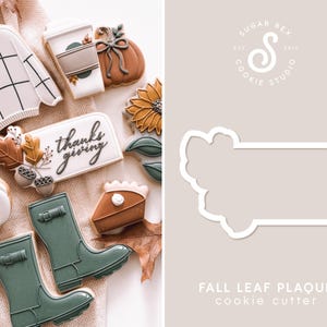 May include: Fall leaf plaque cookie cutter, a white metal cookie cutter shaped like a fall leaf garland. The cutter is on a beige background with the text "FALL LEAF PLAQUE cookie cutter" below it.