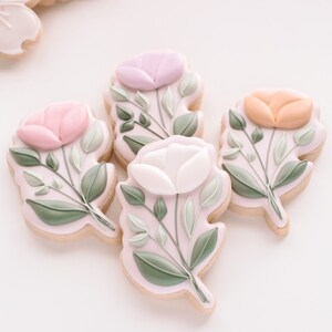 May include: Five decorated sugar cookies with floral designs. Each cookie features a different coloured flower with green leaves. The flowers are pink, purple, white, and orange.