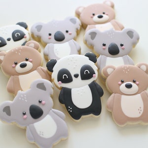 May include: A collection of nine decorated sugar cookies featuring animal designs. The cookies are decorated with brown, black, white, and pink icing. The animals include koalas, pandas, and teddy bears.