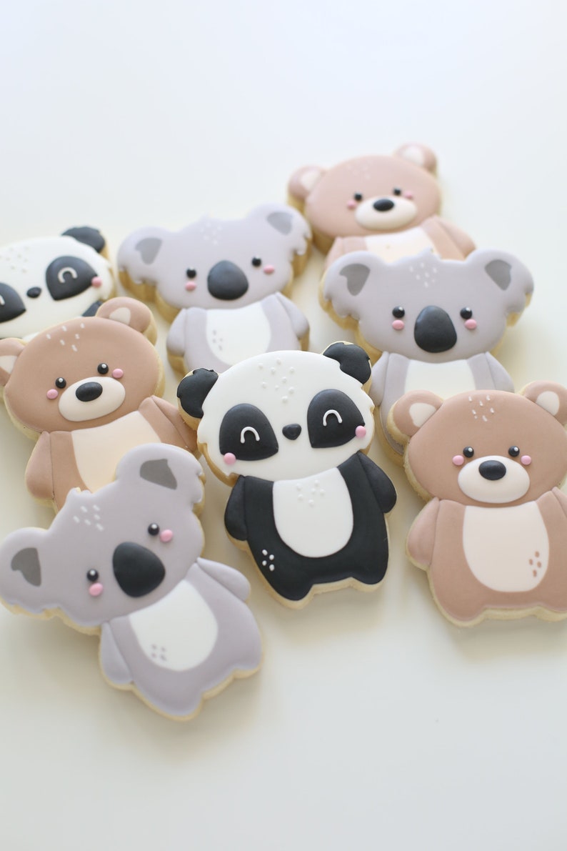 May include: A collection of nine decorated sugar cookies featuring animal designs. The cookies are decorated with brown, black, white, and pink icing. The animals include koalas, pandas, and teddy bears.