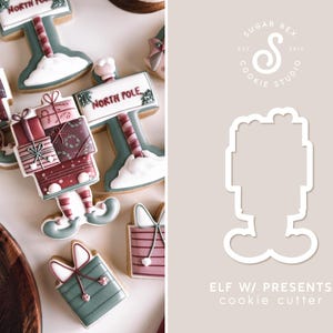 May include: Christmas-themed cookies, including an elf with presents and a North Pole sign. The cookies are decorated with red, green, and white icing. The image also shows a cookie cutter with the text "ELF W/ PRESENTS cookie cutter".