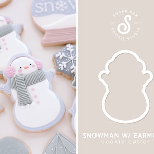 May include: A white cookie cutter shaped like a snowman wearing earmuffs. The cookie cutter is on a light brown background with the text "SNOWMAN W/ EARMUFFS cookie cutter" below it.