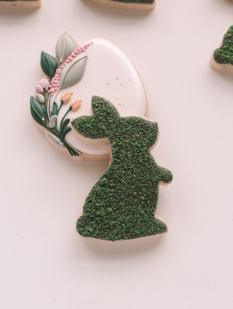 May include: A white and green sugar cookie decorated with a green bunny silhouette and a floral design with pink and yellow accents.