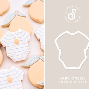K&ouml;nnte beinhalten: Ein Ausstecher in Form eines Baby-Bodys. Der Body ist wei&szlig; und hat ein blaues Streifenmuster. Der Ausstecher befindet sich auf einem hellgrauen Hintergrund mit dem Text "BABY ONESIE cookie cutter" darunter. Der Text "SUGAR REX COOKIE STUDIO EST. 2018" befindet sich in einem Kreis &uuml;ber dem Ausstecher.