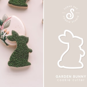 May include: A green bunny cookie cutter with a white outline. The cookie cutter is shaped like a bunny standing on its hind legs with its ears up. The text "GARDEN BUNNY cookie cutter" is below the cookie cutter.