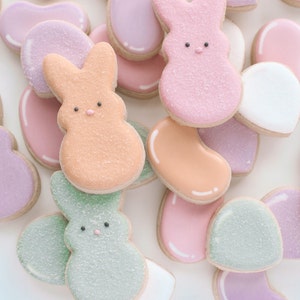 May include: Assortment of pastel-colored sugar cookies decorated with bunny and jelly bean shapes. The cookies are decorated with white, pink, green, and orange icing and sprinkles.
