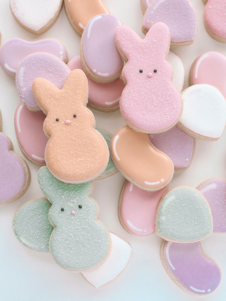 May include: Assortment of pastel-colored sugar cookies decorated with bunny and jelly bean shapes. The cookies are decorated with white, pink, green, and orange icing and sprinkles.