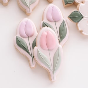 May include: Decorated sugar cookies with pink and green icing. The cookies are shaped like tulips with two tulips on each cookie.