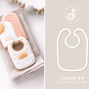 Puede incluir: Dos galletas de az&uacute;car decoradas con un sol y las palabras "Baby Home" y un babero con un dise&ntilde;o de sol. Las galletas est&aacute;n sobre una superficie de lino beige. La imagen tambi&eacute;n muestra un contorno blanco de un cortador de galletas cuadrado para babero sobre un fondo beige con el texto "Square Bib cookie cutter".