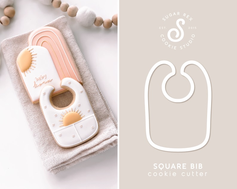 Puede incluir: Dos galletas de az&uacute;car decoradas con un sol y las palabras "Baby Home" y un babero con un dise&ntilde;o de sol. Las galletas est&aacute;n sobre una superficie de lino beige. La imagen tambi&eacute;n muestra un contorno blanco de un cortador de galletas cuadrado para babero sobre un fondo beige con el texto "Square Bib cookie cutter".