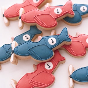 May include: A collection of red and blue airplane-shaped cookies decorated with white icing and the number "1".