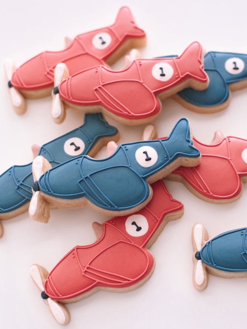 May include: A collection of red and blue airplane-shaped cookies decorated with white icing and the number "1".