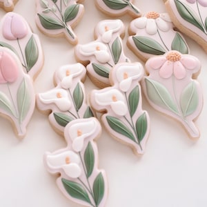 May include: A collection of decorated sugar cookies featuring various floral designs. The cookies are decorated with pink, white, and green icing, and each cookie features a different flower, including tulips, lilies, and daisies.