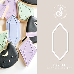 May include: A set of purple, green, and blue crystal cookie cutters. The cutters are shaped like various geometric crystals. The image also includes a black cat cookie cutter and a white logo for Sugar Rex Cookie Studio.