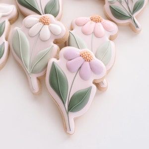 May include: A collection of decorated sugar cookies featuring a floral design. The cookies are decorated with white, pink, and purple flowers with green leaves.