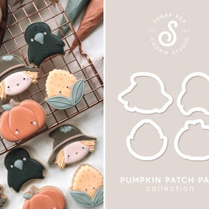 May include: A set of cookie cutters for making pumpkin patch themed cookies. The cutters are in the shape of a pumpkin, a scarecrow, a crow, and a corn stalk. The cutters are made of white metal and are shown on a light gray background. PUMPKIN PATCH PALS collection is written below the cutters.