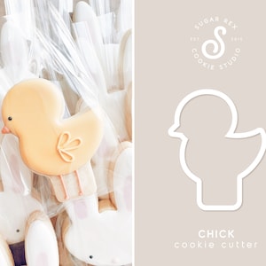 May include: An Easter-themed image featuring a yellow chick-shaped cookie with orange details, packaged in clear cellophane. The cookie cutter outline is also shown, with the text "CHICK cookie cutter" and the Sugar Rex Cookie Studio logo.
