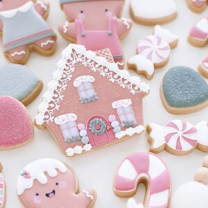 Pu&ograve; includere: Una collezione di biscotti di pan di zenzero rosa e grigi decorati con glassa e codette. I biscotti hanno la forma di omini di pan di zenzero, case, bastoncini di zucchero e cuori.