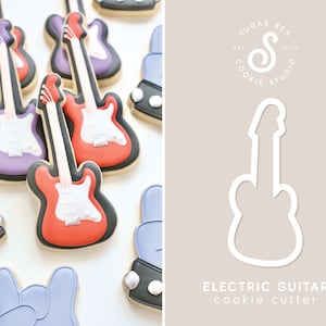 May include: A cookie cutter in the shape of an electric guitar. The cutter is white and is shown on a light brown background. The text "ELECTRIC GUITAR cookie cutter" is below the cutter.