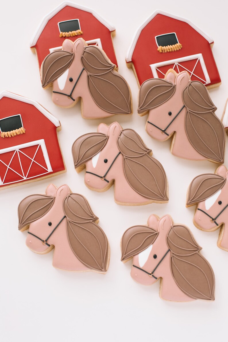 Pu&ograve; includere: Un set di biscotti di zucchero decorati con fienili rossi e cavalli marroni. I biscotti sono decorati con glassa bianca e dettagli neri.