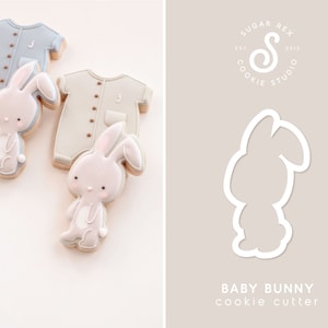 May include: A cookie cutter in the shape of a baby bunny. The cutter is white and is shown against a light gray background. The text "BABY BUNNY cookie cutter" is below the cutter.