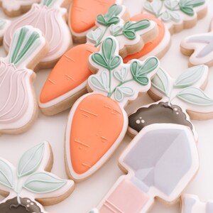 Puede incluir: Un conjunto de galletas de az&uacute;car decoradas con un tema de jard&iacute;n. Las galletas est&aacute;n decoradas con hojas verdes, zanahorias naranjas, cebollas rosas y una pala morada.