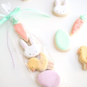 May include: A clear plastic bag filled with Easter-themed sugar cookies. The cookies are decorated with pastel icing and include a carrot, a bunny, a chick, and two eggs.