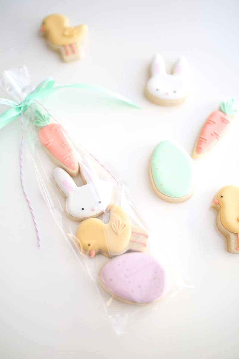 May include: A clear plastic bag filled with Easter-themed sugar cookies. The cookies are decorated with pastel icing and include a carrot, a bunny, a chick, and two eggs.