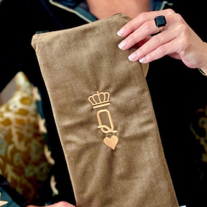 May include: A brown velvet pouch with a gold embroidered crown and the letter "Q" with a heart. The pouch has a white label with the word "quiver" printed on it.