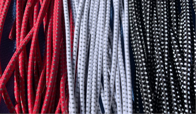May include: Close-up of several strands of elastic cord in red, white, and black. The cords have a dotted pattern and are tightly packed together. The cords are likely used for crafting or other DIY projects.