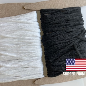 May include: Two spools of elastic cord, one white and one black, are wrapped around cardboard spools. The spools are sitting on a brown surface. "SHIPPED FROM USA" is printed on the surface.