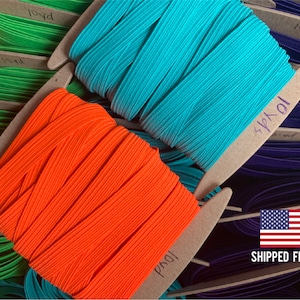 May include: Close-up of spools of colorful elastic cord. The spools are labeled with the length in yards. The colors are orange, turquoise, green, and purple.