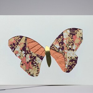 May include: A white card with a paper butterfly cutout. The butterfly is made of purple, orange, and gold patterned paper.
