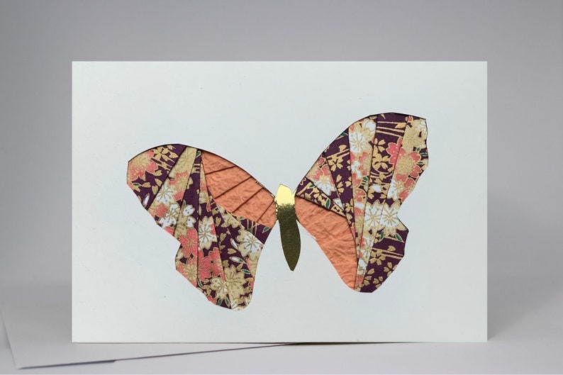 May include: A white card with a paper butterfly cutout. The butterfly is made of purple, orange, and gold patterned paper.