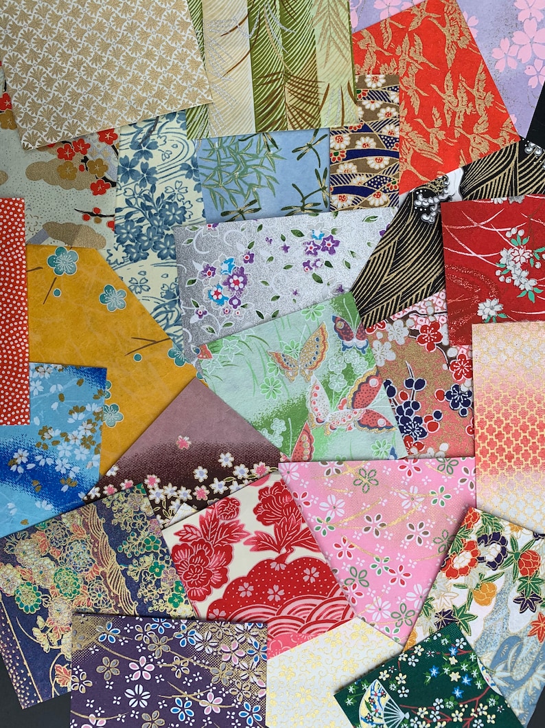 May include: Assortment of colorful patterned Japanese washi paper squares. The paper features various floral, geometric, and abstract designs in shades of pink, blue, green, red, and gold.
