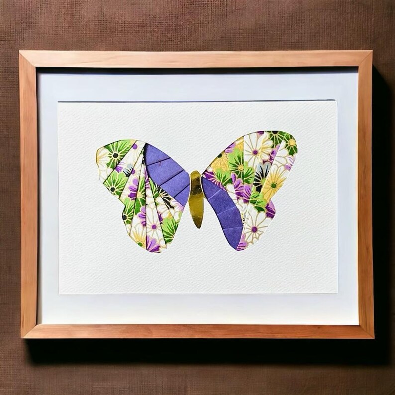 May include: A framed artwork featuring a colorful butterfly made of paper. The butterfly has purple, green, and gold accents and is set against a white background.