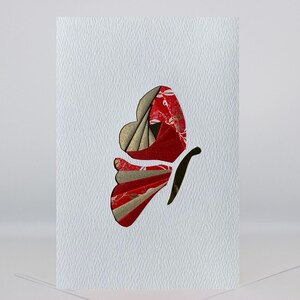 May include: A white card with a red and gold butterfly made of paper. The butterfly is cut out of the card and has a textured surface.