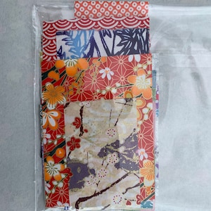 May include: A clear plastic bag containing a stack of colorful patterned Japanese papers. The papers feature floral, geometric, and wave designs in shades of red, blue, gold, and white.