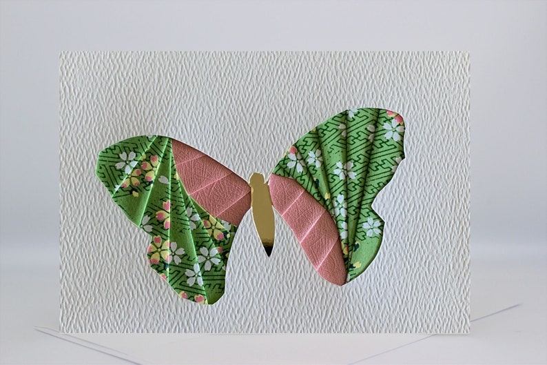 May include: A green and pink butterfly origami card with a white background. The butterfly is made of patterned paper and has a gold body.